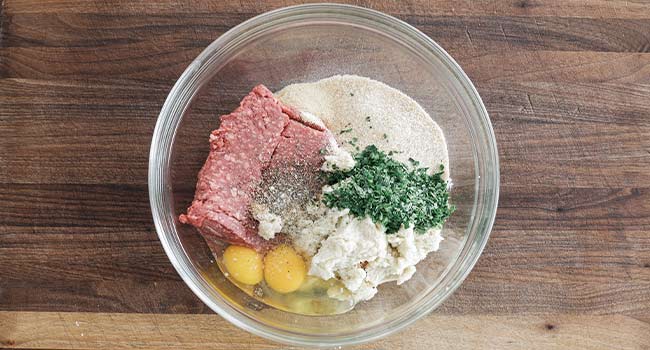 adding meatball ingredients to a bowl