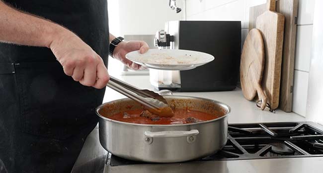 adding ribs to a pot of tomato sauce