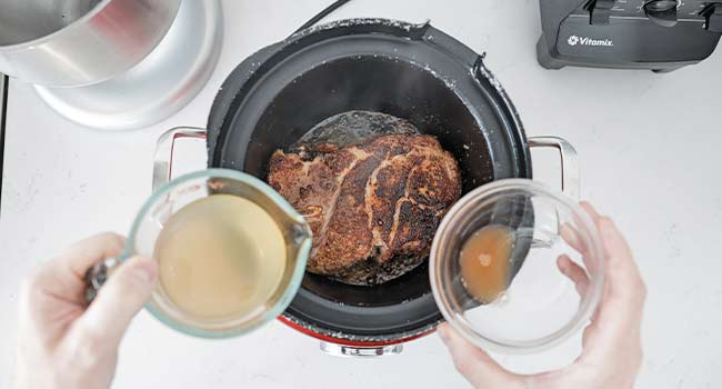 adding stock and vinegar to a slow cooker with pork