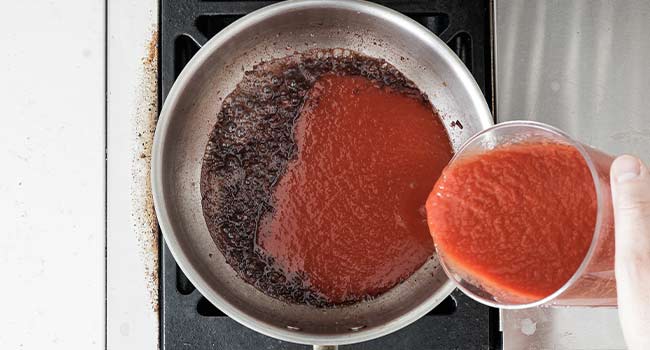 adding tomato puree to a pot of sauce