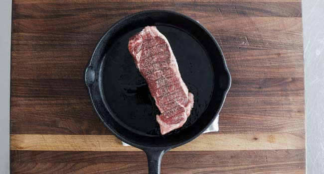 adding a steak to a pan of oil