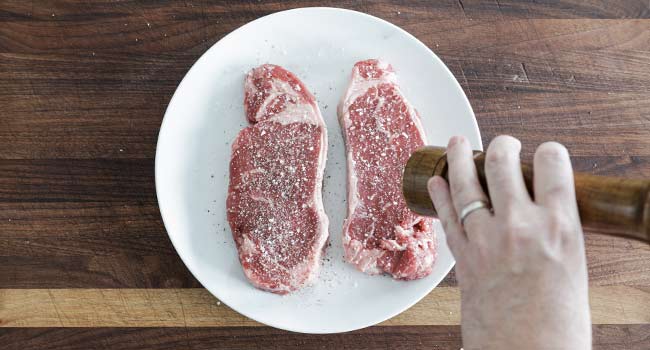 seasoning steaks with salt and pepper