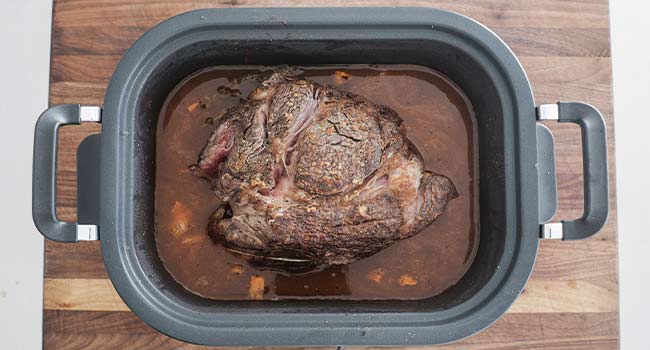 adding beef and herbs to a slow cooker of broth