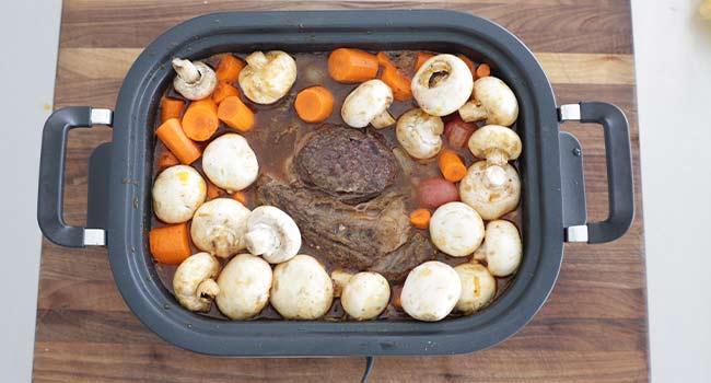 adding veggies to a slow cooker pot roast