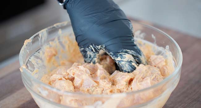 mixing chicken into a masala marinade