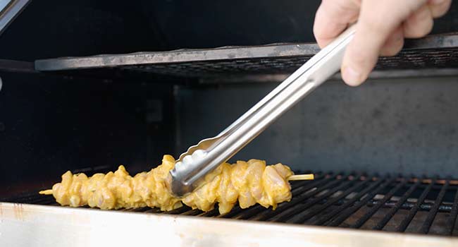 adding skewered chicken to a grill