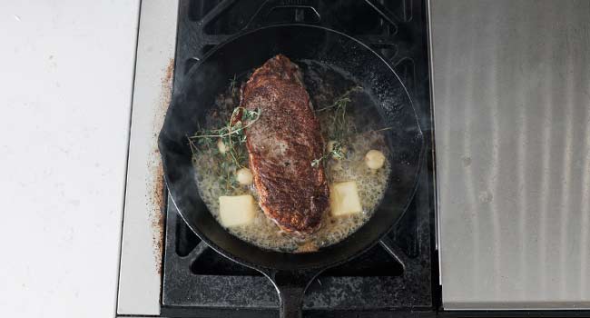 steak in a pan with butter, herbs, and garlic