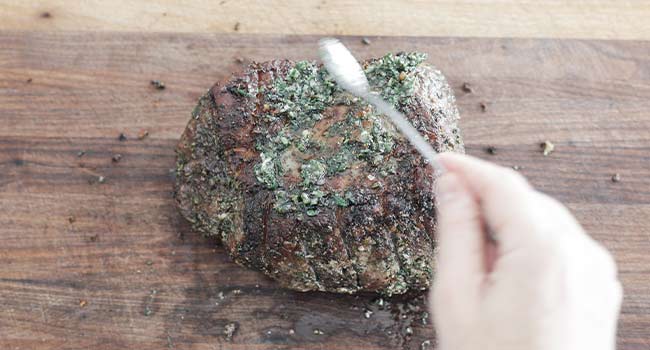 adding more herb and garlic oil to a cooked beef roast