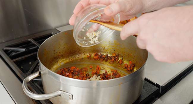 adding garlic to a pan of peppers and onions