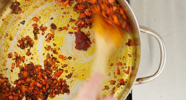 adding tomato paste to a pan of peppers and onions