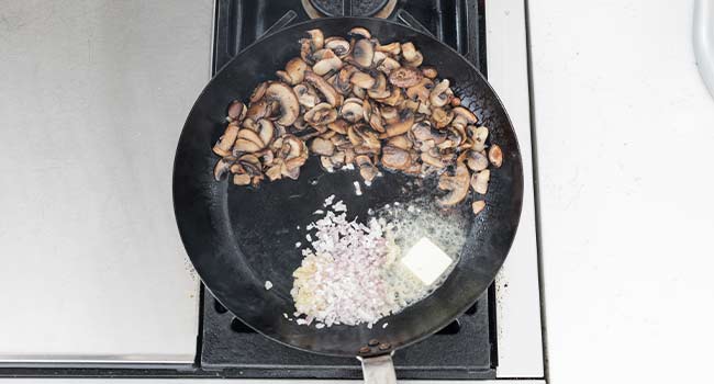 adding butter, garlic, and shallots to a pan of mushrooms