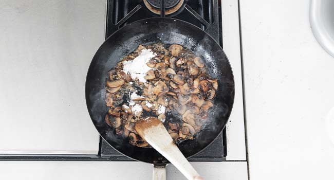 sprinkling flour on cooked mushrooms