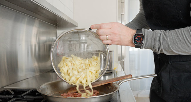 adding cooked pasta to a pan