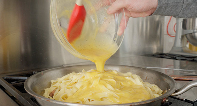 adding pasta alla papalina sauce to pasta