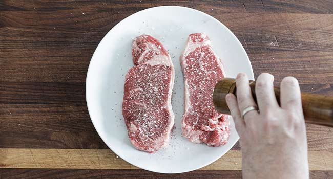 seasoning steaks with salt and pepper