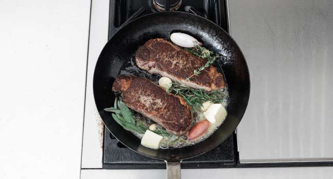 adding butter and herbs to a pan with steaks