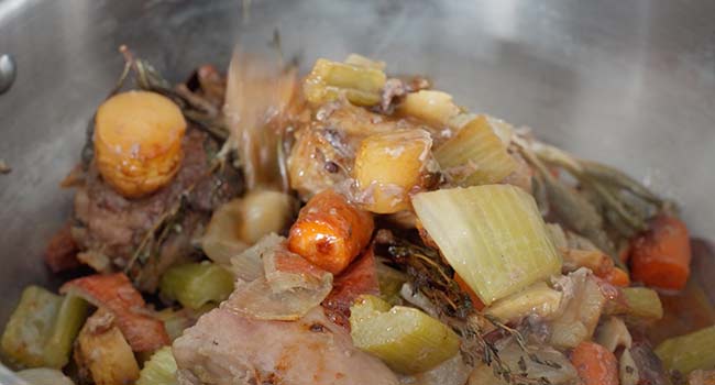 adding roasted veggies and turkey parts to a pot