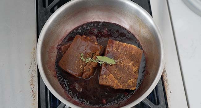 adding demi-glace and herbs to a pot of wine