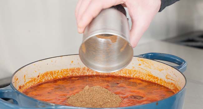 adding spices to a pot of chili