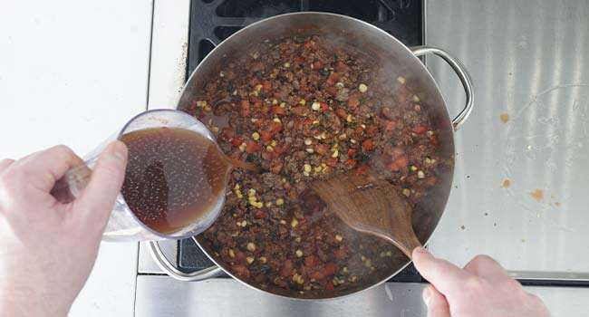 adding beef stock to a pot of goulash