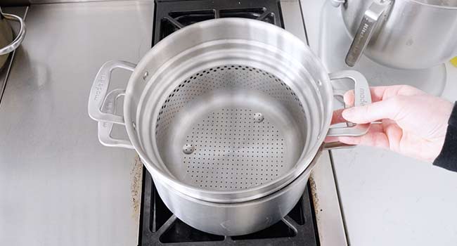 adding a basket to boiling water in a pot