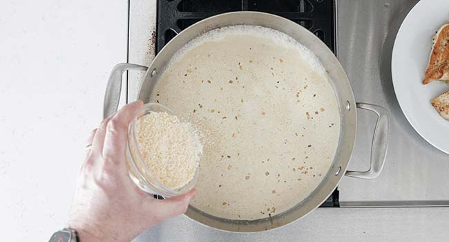 adding cheese to a pan of cream sauce