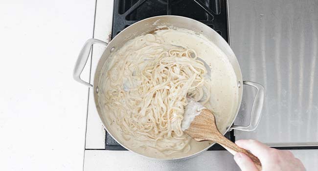 coating cooked pasta in alfredo sauce